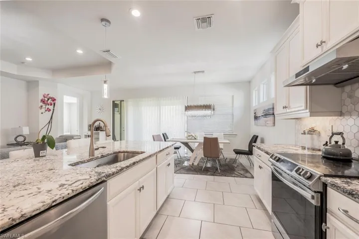 Kitchen with stainless steel appliances, white cabinetry, hanging light fixtures, light stone counters, and open floor plan