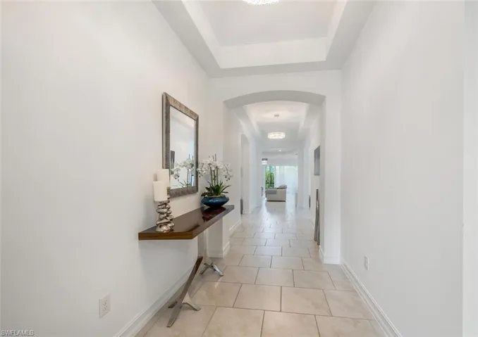 Corridor featuring a tray ceiling, arched walkways, and light tile patterned flooring