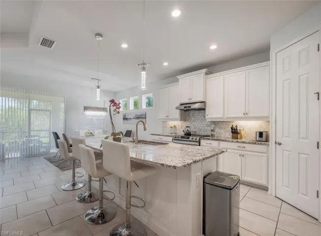 Kitchen with a kitchen breakfast bar, pendant lighting, white cabinetry, and light stone countertops