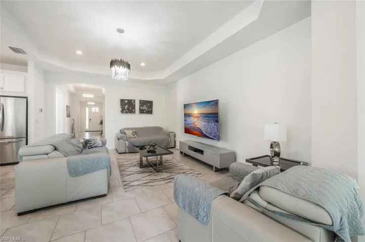 Living room with a raised ceiling, light tile patterned flooring, and suspended lighting