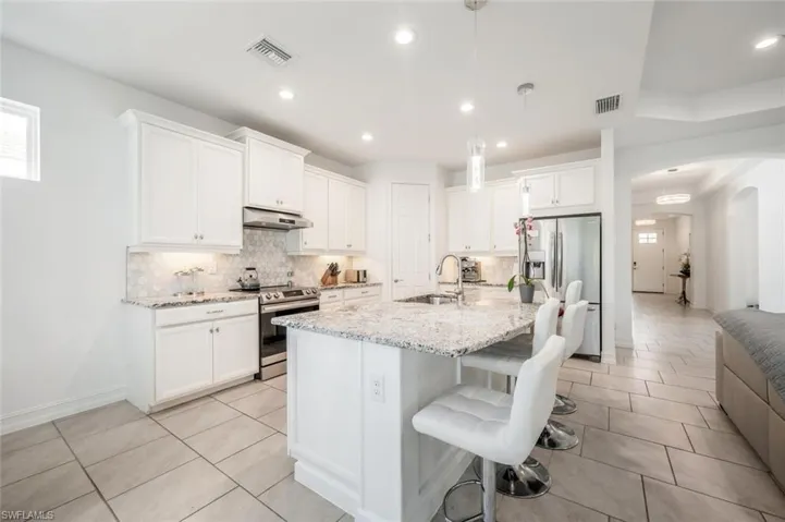 Kitchen featuring arched walkways, decorative light fixtures, white cabinets, and a breakfast bar area