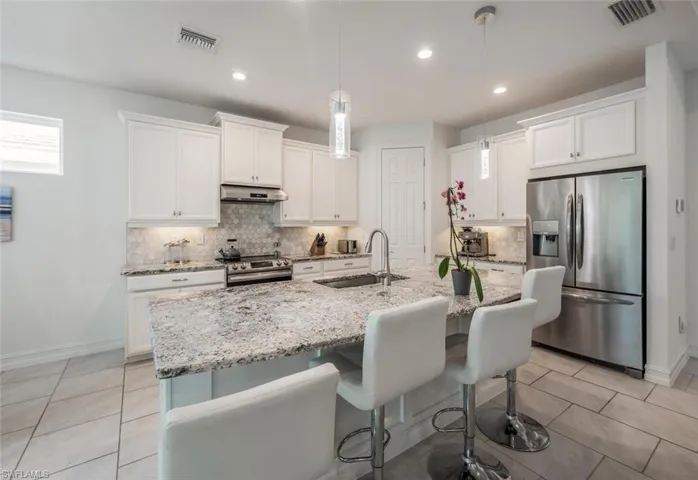 Kitchen with stainless steel appliances, a kitchen breakfast bar, white cabinetry, light stone counters, and hanging light fixtures