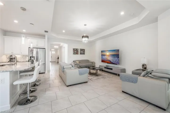 Living area featuring arched walkways, a raised ceiling, light tile patterned floors, and suspended lighting