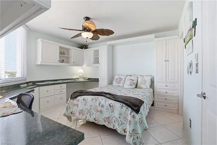 Bedroom with light tile patterned floors, ceiling fan, and built in study area - Virtually Edited Image