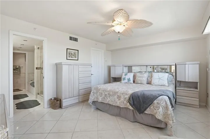 Bedroom featuring ceiling fan, light tile patterned floors, and ensuite bath - Virtually Edited Image