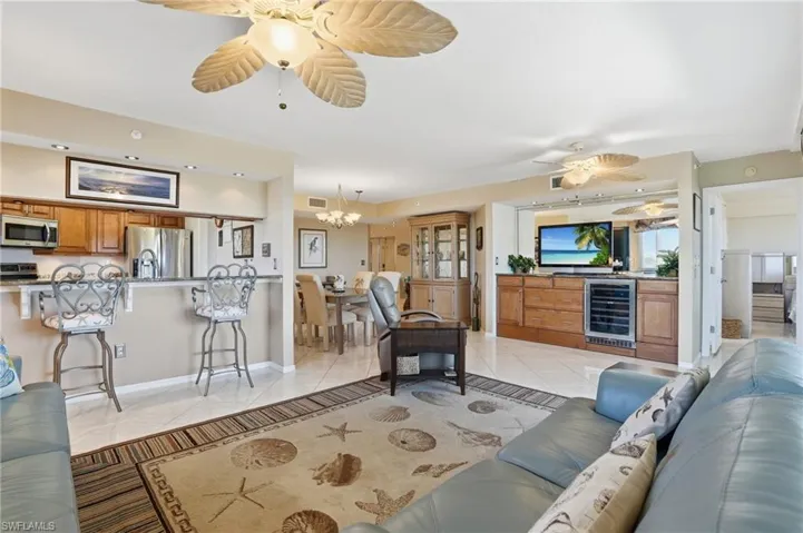 Living room featuring a ceiling fan, wine cooler, light tile patterned floors, and suspended lighting - Virtually Edited Image