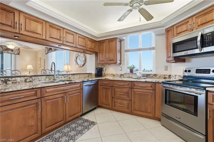 Kitchen with ceiling fan, stainless steel appliances, wood finish cabinetry, ornamental molding, and light stone countertops - Virtually Edited Image