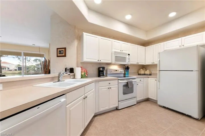 Kitchen with white appliances, white cabinets, light countertops, recessed lighting, and light tile patterned flooring
