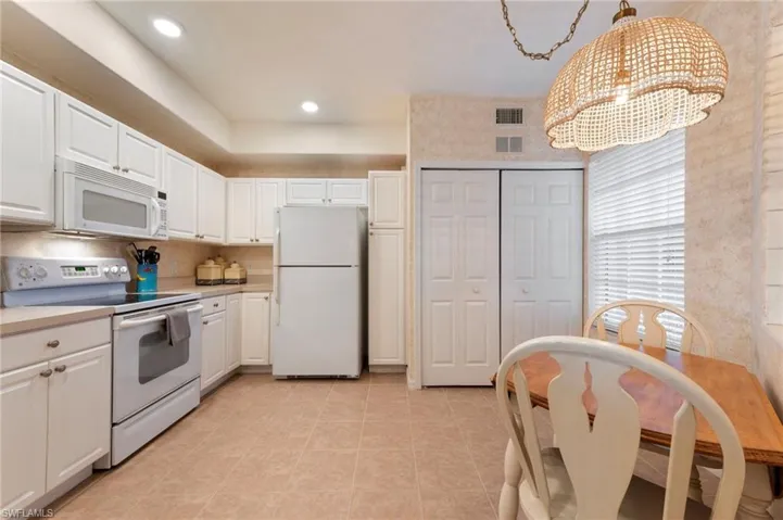 Kitchen with white appliances, light countertops, white cabinetry, decorative light fixtures, and a chandelier