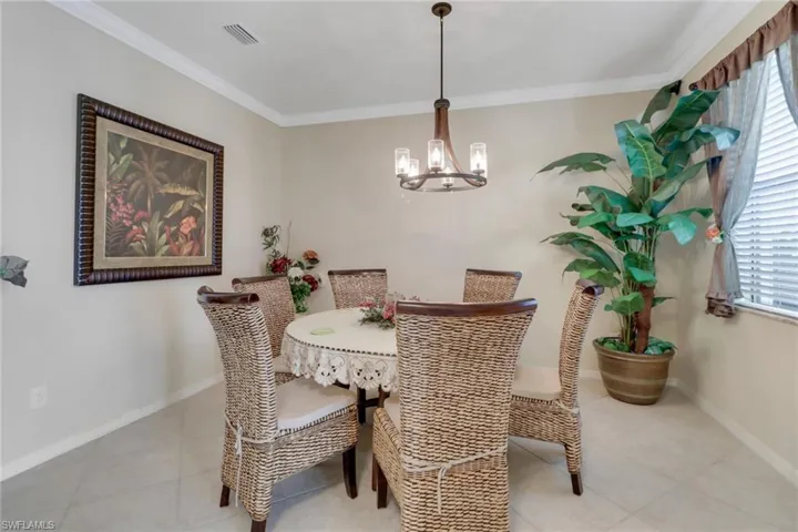 Dining room with ornamental molding, light tile patterned flooring, and an inviting chandelier