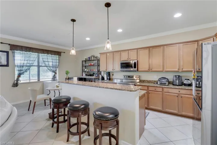 Kitchen featuring light brown cabinets, appliances with stainless steel finishes, pendant lighting, and light stone countertops