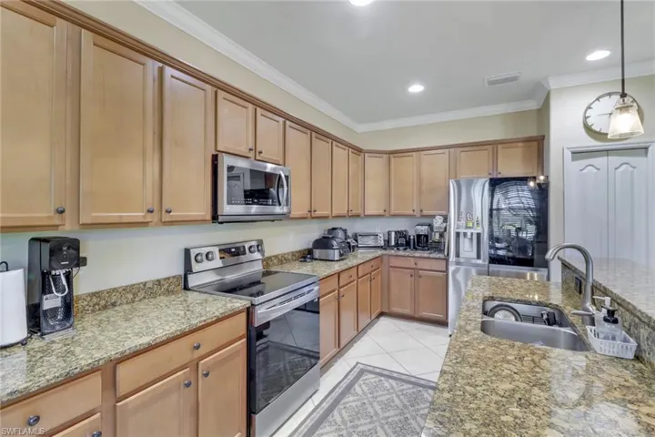 Kitchen featuring light stone counters, light tile patterned floors, stainless steel appliances, ornamental molding, and sink