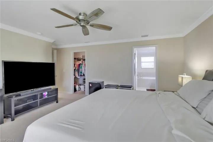 Bedroom featuring ceiling fan, a walk in closet, ensuite bathroom, ornamental molding, and light colored carpet