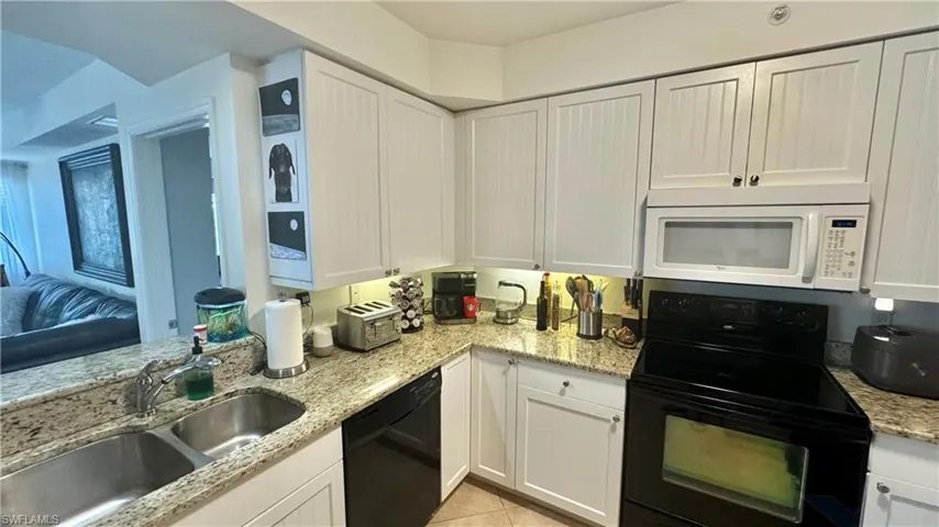 Kitchen featuring sink, white cabinetry, black appliances, light tile patterned floors, and light stone countertops