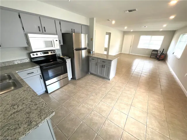 Kitchen featuring gray cabinetry, appliances with stainless steel finishes, light tile patterned floors, a peninsula, and open floor plan
