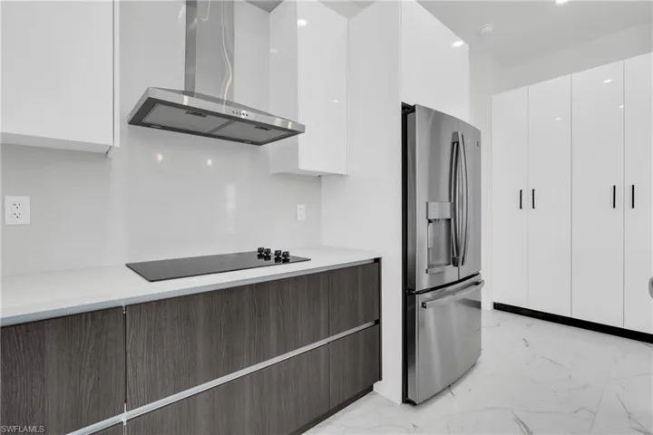 Kitchen featuring stainless steel refrigerator with ice dispenser, marble finish floor, wall chimney exhaust hood, and black electric cooktop