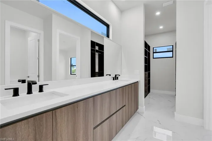 Full bathroom with baseboards, a sink, marble finish floor, and double vanity