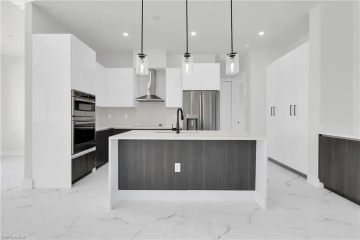Kitchen featuring marble finish floor, modern cabinets, wall chimney exhaust hood, a sink, and stainless steel appliances