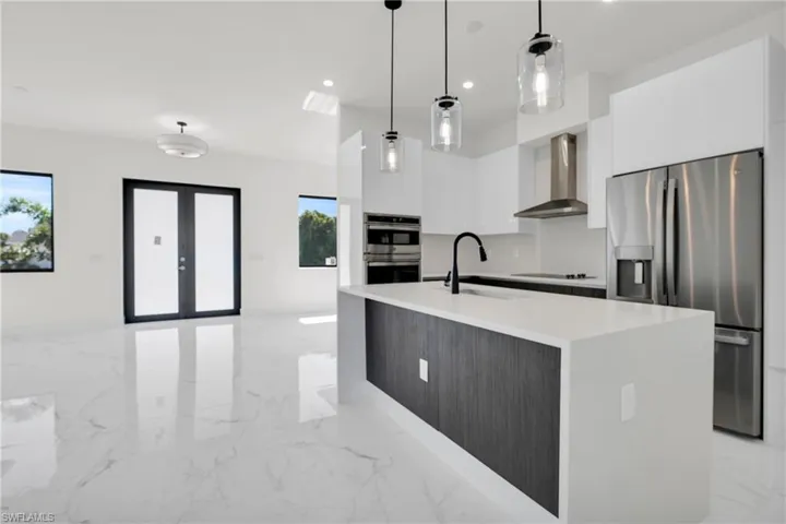 Kitchen with appliances with stainless steel finishes, modern cabinets, a sink, marble finish floor, and wall chimney exhaust hood