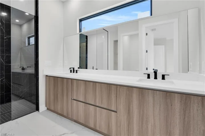Full bath featuring double vanity, a sink, marble finish floor, and a marble finish shower