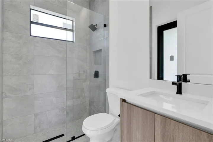 Full bath with toilet, tiled shower, and vanity