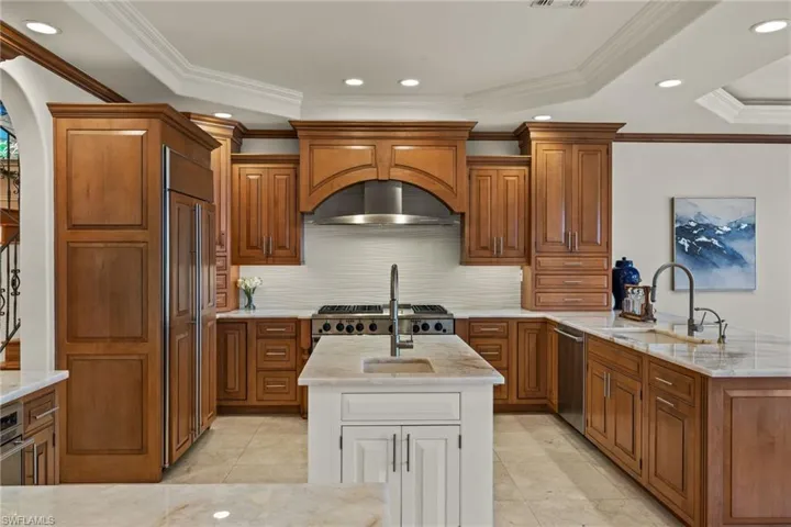 Kitchen featuring a center island with sink, arched walkways, brown cabinets, and dishwasher