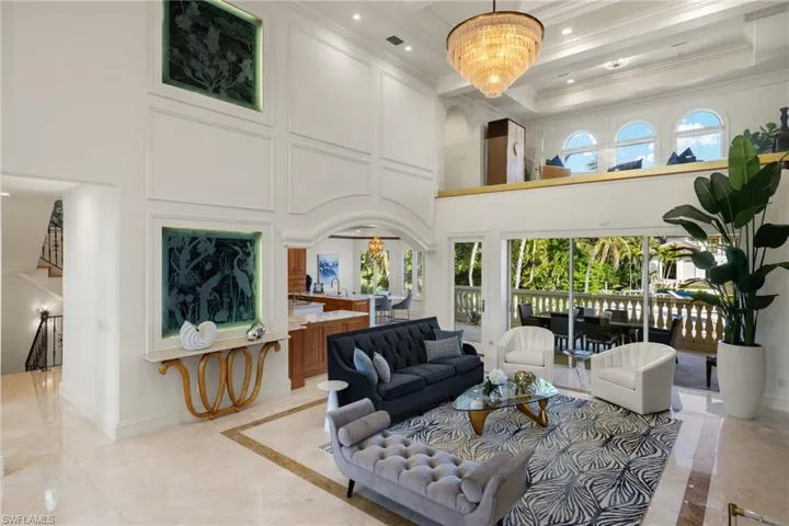 Living room featuring baseboards, a towering ceiling, ornamental molding, an inviting chandelier, and recessed lighting
