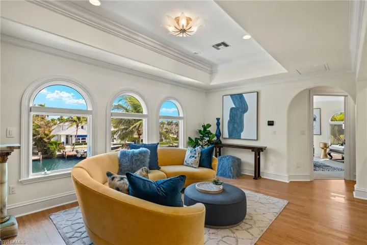 Sitting room featuring visible vents, arched walkways, a raised ceiling, wood finished floors, and crown molding