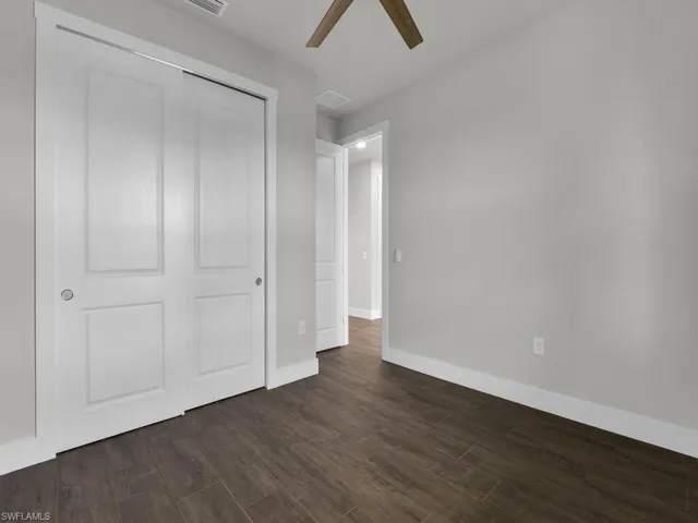 Unfurnished bedroom featuring dark wood-type flooring, a closet, and a ceiling fan
