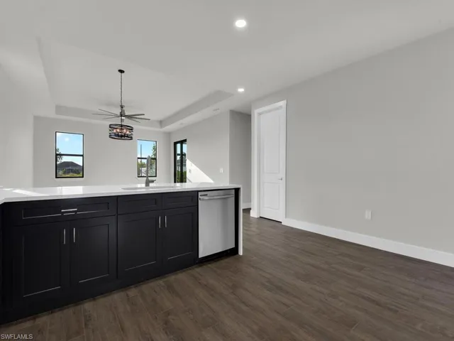 Kitchen with dark cabinets, stainless steel dishwasher, dark wood-style flooring, open floor plan, and a raised ceiling