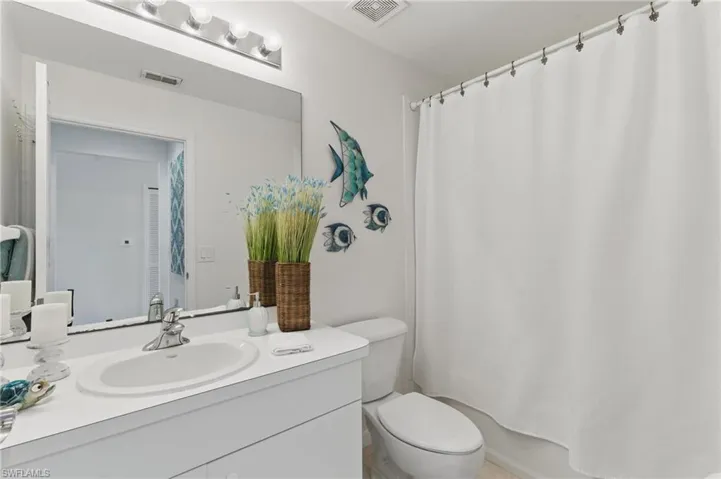 Full bath with toilet, vanity, shower / tub combo with curtain, and visible vents