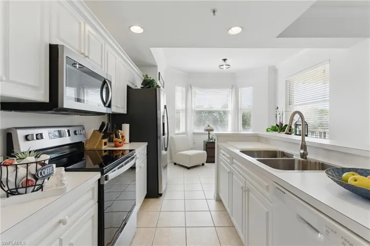 Kitchen featuring a sink, white cabinetry, light tile patterned floors, stainless steel appliances, and ornamental molding