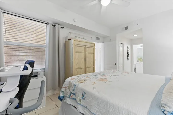 Bedroom featuring light tile patterned flooring, visible vents, ensuite bathroom, and a ceiling fan