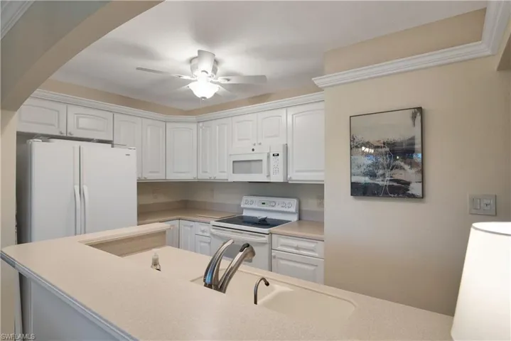 Kitchen with white appliances, white cabinetry, a ceiling fan, and arched walkways