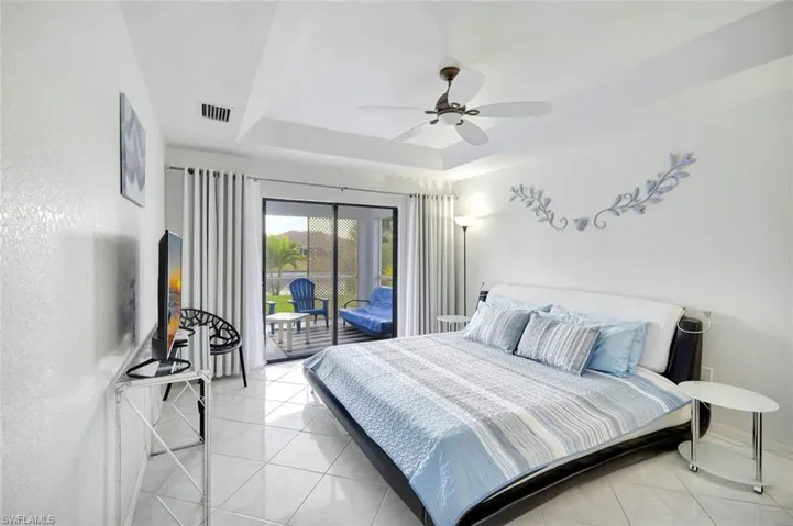 Bedroom with a raised ceiling, access to exterior, light tile patterned flooring, and a ceiling fan