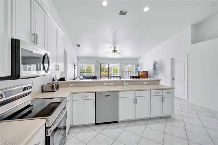Kitchen with appliances with stainless steel finishes, white cabinets, open floor plan, light countertops, and vaulted ceiling