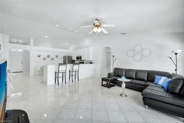 Living room with arched walkways, lofted ceiling, light tile patterned floors, a ceiling fan, and recessed lighting