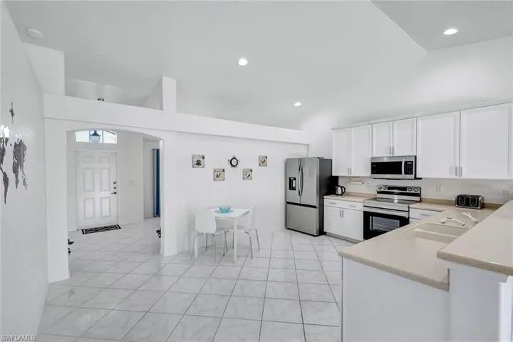 Kitchen featuring stainless steel appliances, white cabinets, vaulted ceiling, arched walkways, and recessed lighting