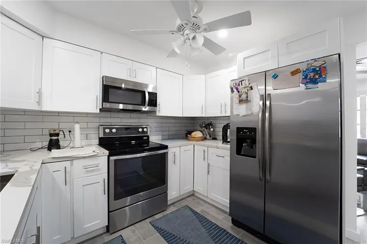 Kitchen featuring decorative backsplash, white cabinets, light stone counters, and appliances with stainless steel finishes