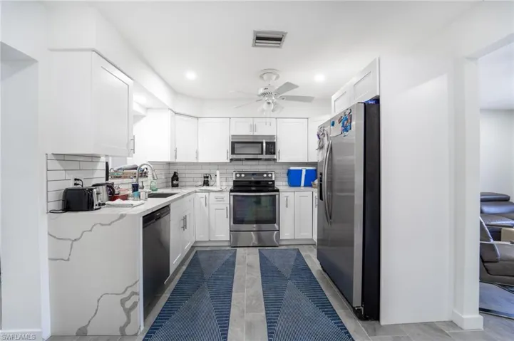 Kitchen with sink, ceiling fan, tasteful backsplash, white cabinetry, and stainless steel appliances