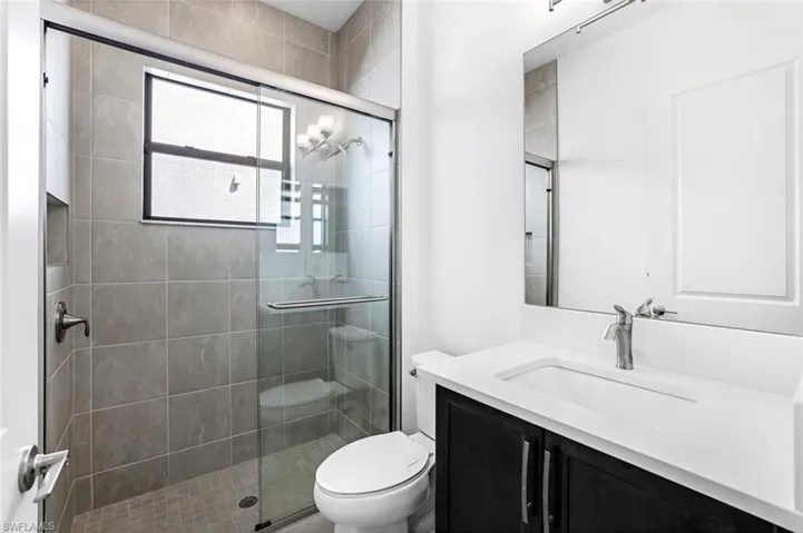 Bathroom featuring a shower with door, vanity, and toilet
