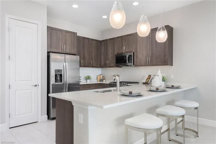 Kitchen with dark brown cabinets, appliances with stainless steel finishes, pendant lighting, and a kitchen breakfast bar