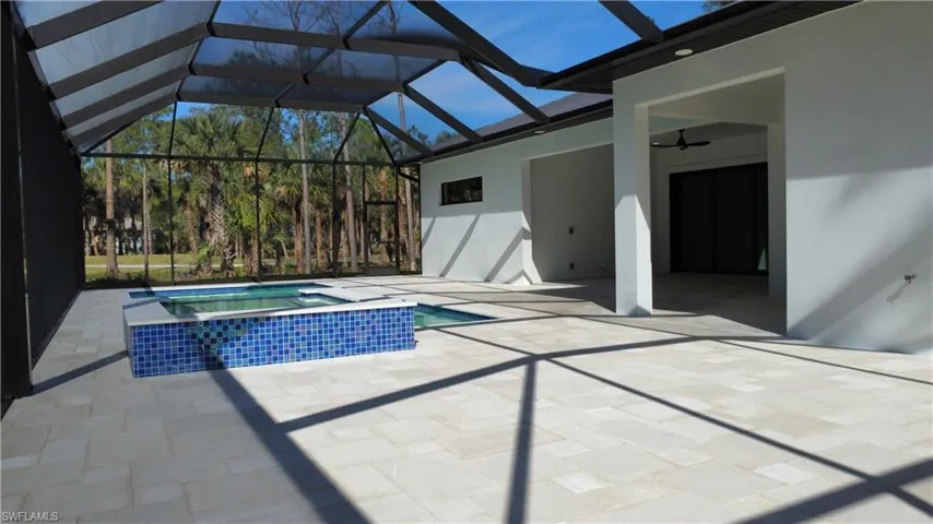 View of swimming pool with ceiling fan, a patio area, glass enclosure, and an in ground hot tub