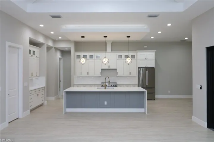 Kitchen featuring an island with sink, white cabinetry, stainless steel refrigerator, and hanging light fixtures
