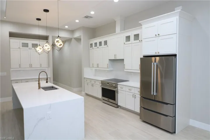 Kitchen featuring white cabinets, decorative light fixtures, stainless steel appliances, sink, and light stone counters