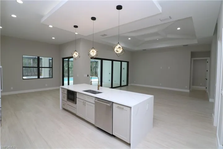 Kitchen with dishwasher, hanging light fixtures, sink, white cabinets, and light stone counters