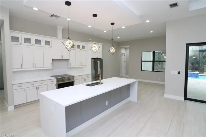 Kitchen with high quality appliances, decorative light fixtures, white cabinets, sink, and a center island with sink