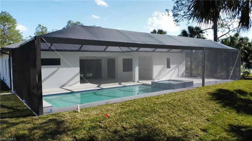 Rear view of property with a patio area, a pool with hot tub, glass enclosure, and a lawn