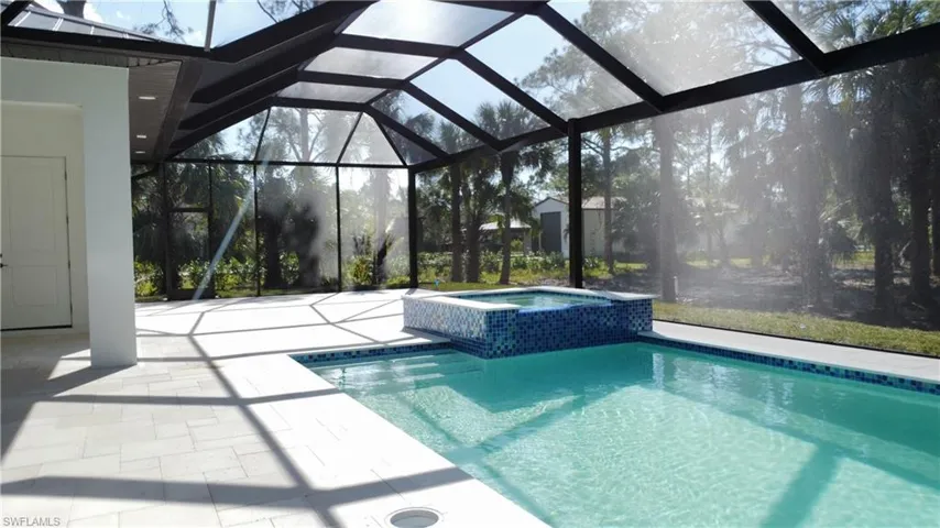 View of pool with an in ground hot tub, glass enclosure, and a patio area