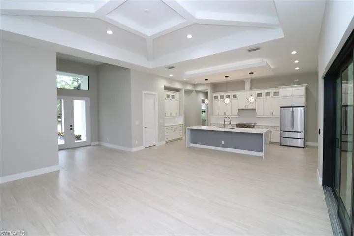 Kitchen with a spacious island, decorative light fixtures, sink, white cabinets, and stainless steel refrigerator